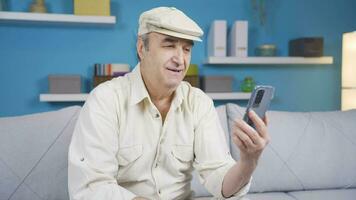 Elderly grandpa sitting on sofa enjoying online on mobile phone web app. video