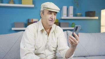 Elderly grandpa sitting on sofa enjoying online on mobile phone web app. video