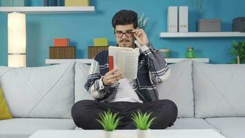 joven hombre con lentes es leyendo un libro a hogar. video