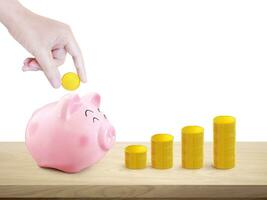 Hand puts gold coins into a piggy bank and a pile of gold coins on a wooden table. white background photo