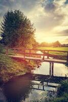 Wooden bridge over small river at sunset. photo