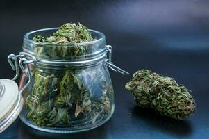 noir still life with glass mason jar full of dry medical cannabis buds on black background photo