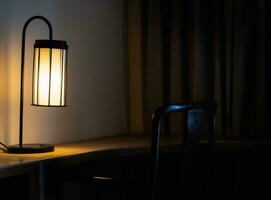 Glowing desk lamp on wooden table in the dark bedroom photo