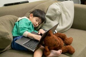 asiático chico dormido mientras estudiando en línea en ordenador portátil foto