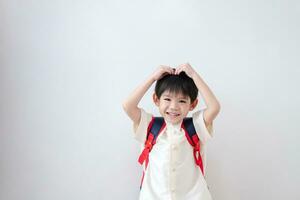 Asian boy Wearing traditional Thai clothing, standing with a school bag. Make a heart gesture on his head preparing to go to school on a white background photo