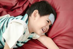 Asian boy Lying sick with a fever reducing patch on her forehead but still smiling. photo