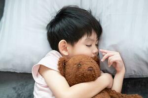 A boy is sleeping and hugging a teddy bear in bed. photo