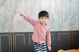 An Asian boy stands with his hands pointing to the side. photo