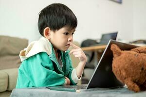 asiático chico estudiando en línea y haciendo ocupaciones en ordenador portátil foto
