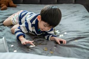 asiático chico felizmente contando monedas a salvar dinero foto