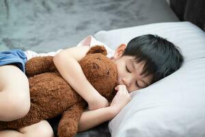 un chico es dormido y abrazando un osito de peluche oso en cama. foto