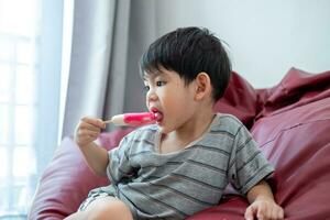 un asiático chico es comiendo delicioso hielo crema en un silla. foto