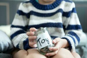 Asian boy sitting holding a glass jar full of coins, saving money to buy toys. photo