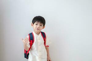 Asian boy Wearing traditional Thai clothing, standing with a school bag. Make a beckoning gesture preparing to go to school on a white background photo