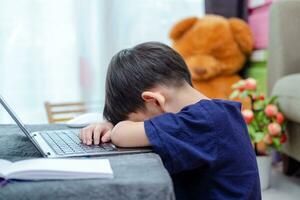 asiático chico dormido mientras estudiando en línea en ordenador portátil foto