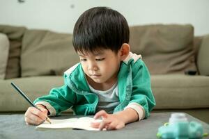 un chico es dibujo imágenes en un cuaderno en el mesa. aprendizaje fuera de el salón de clases foto