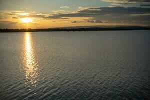 puesta de sol terminado el reservorio el del sol rayos golpear el superficie de el agua. foto