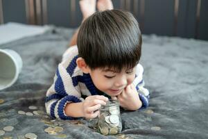 asiático chico felizmente contando monedas a salvar dinero foto