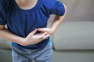 un chico con dolor en su estómago frota su estómago en el dolor punto. foto