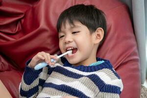 asiático chico cepillado su dientes en el vivo habitación foto