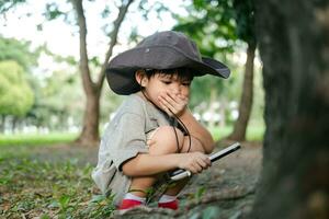 Asian boy wearing a hat in a forest exploration suit Use a magnifying glass to survey the tree area. photo