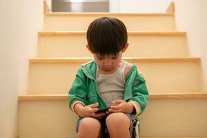 un chico quien estaba regañado por su madre secretamente llegó a jugar en el teléfono en el escaleras. foto