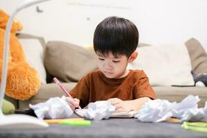 asiático chico dibujo en mesa y allí estaba un pedazo de papel izquierda en el mesa. foto