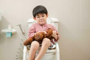asiático chico sentado en el baño cuenco en mano participación osito de peluche oso foto