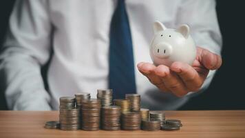 Human holds a piggy bank and there are coins lined up on the wooden floor. Concepts of finance, savings, investment, and setting goals for fixed deposits with banks. photo