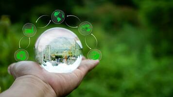 Concept of renewable energy,  renewable energy sources. An image of a building under construction in crystal glass resting on a person's hand and with a natural green background. photo