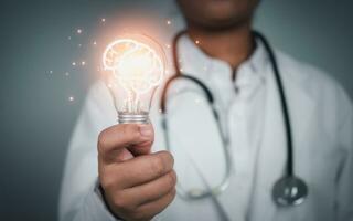 Doctor holding Light bulb with brain icon inside on grey background. Medical health care and medical services. Technology of medical service. photo