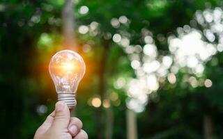 Human hand holds a light bulb with natural bokeh background. Idea, innovation and inspiration concept, creative concept,  earth day or protection of environment, save energy of the world. photo