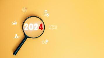 Magnifying glass focused on letter 2024 on yellow background. Represents setting goals for 2024, Startup concept. Financial planning, development, Business strategy, Setting business goals. photo