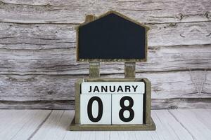 Chalkboard with January 08 date on white cube block on wooden table. photo