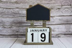 Chalkboard with January 19 date on white cube block on wooden table. photo