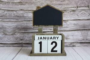 Chalkboard with January 12 date on white cube block on wooden table. photo