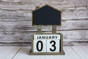 Chalkboard with January 03 date on white cube block on wooden table. photo