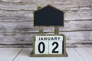 Chalkboard with January 02 date on white cube block on wooden table. photo