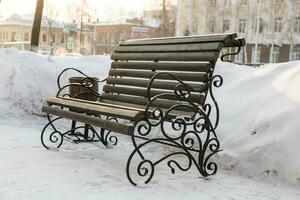 Bench in park with snow in winter season. City and town street concept photo