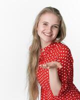 Smiling blond woman stretches her one palm to camera. Portrait of model in red polka dot dress photo