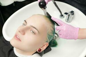 High-angle shot of head young woman in sink. Hairdresser washing green hair of customer with shampoo using special shower. photo