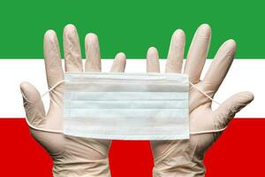 Paramedic holding respiratory face mask in two hands in white gloves on background flag of Islamic Republic of Iran photo