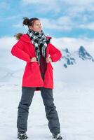 Woman tourist dressed in red winter jacket, sports pants, trekking boots stands in winter mountains photo