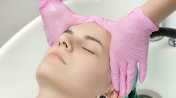 Head of young woman with closed eyes in sink in hair salon. Hairdresser hands in gloves washing hair in beauty salon photo