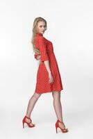 Young blonde female in red polka dot dress standing and looking over shoulder on white background photo