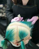 Top view of head of young woman with green hair and bleached hair roots in professional beauty salon photo