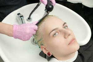 peluquero en protector guante peinada verde pelo de cliente, mientras Lavado pelo en ducha en especial lavabo foto