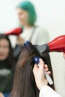 Hands of hairstylist drying brunette hair of customer using hair dryer and comb in beauty salon photo