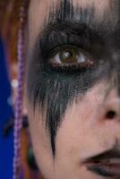 Closeup half of young woman face with spooky black stage make up. Studio shot of dramatic portrait photo