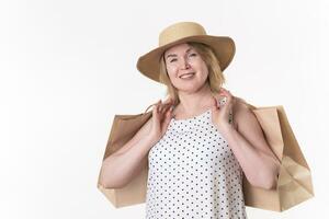 Cheerful woman shopper holds paper craft shopping bags in hands. Female 49 years old in white dress photo